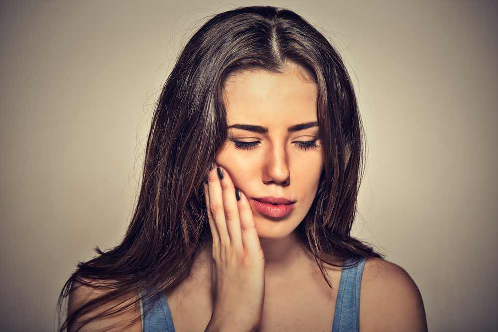 woman holding side of mouth in pain